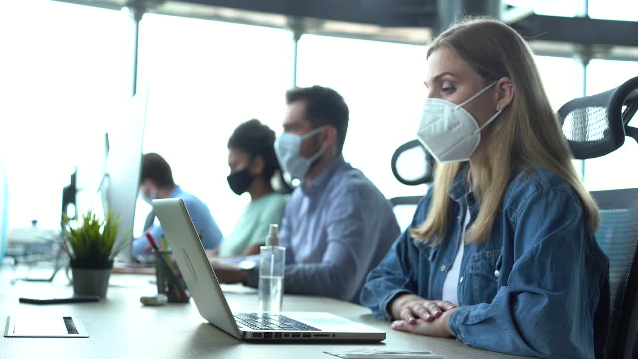 一名妇女戴着医用口罩坐在办公室清洁电脑键盘视频素材
