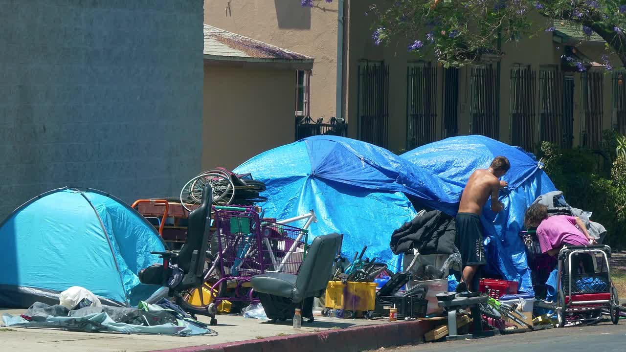 在加州洛杉矶，无家可归危机和新冠肺炎大流行期间，汽车经过住在帐篷里的无家可归者和精神病患者，4K视频下载
