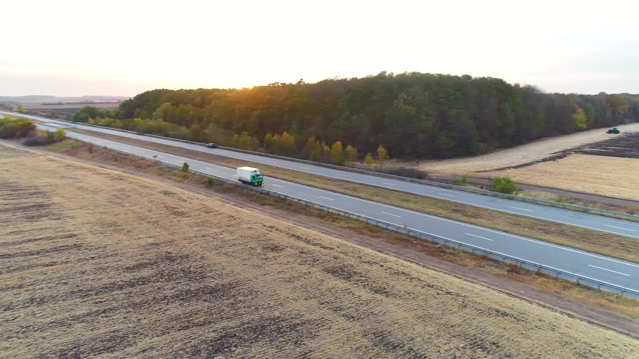 日落时分，卡车在田野间的公路上行驶。卡车行驶在一条笔直的道路上，夕阳俯视图视频素材