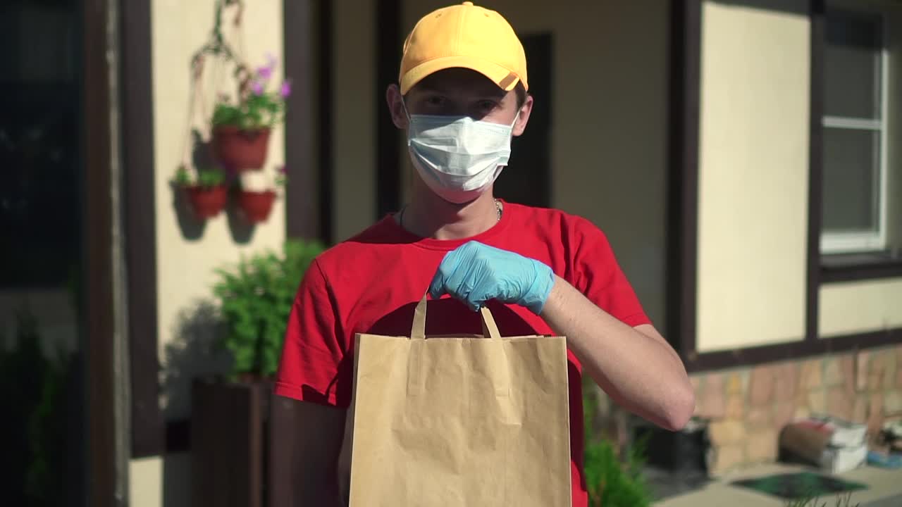 年轻的快递员与纸袋在他的手在背景的房子户外spbd视频下载