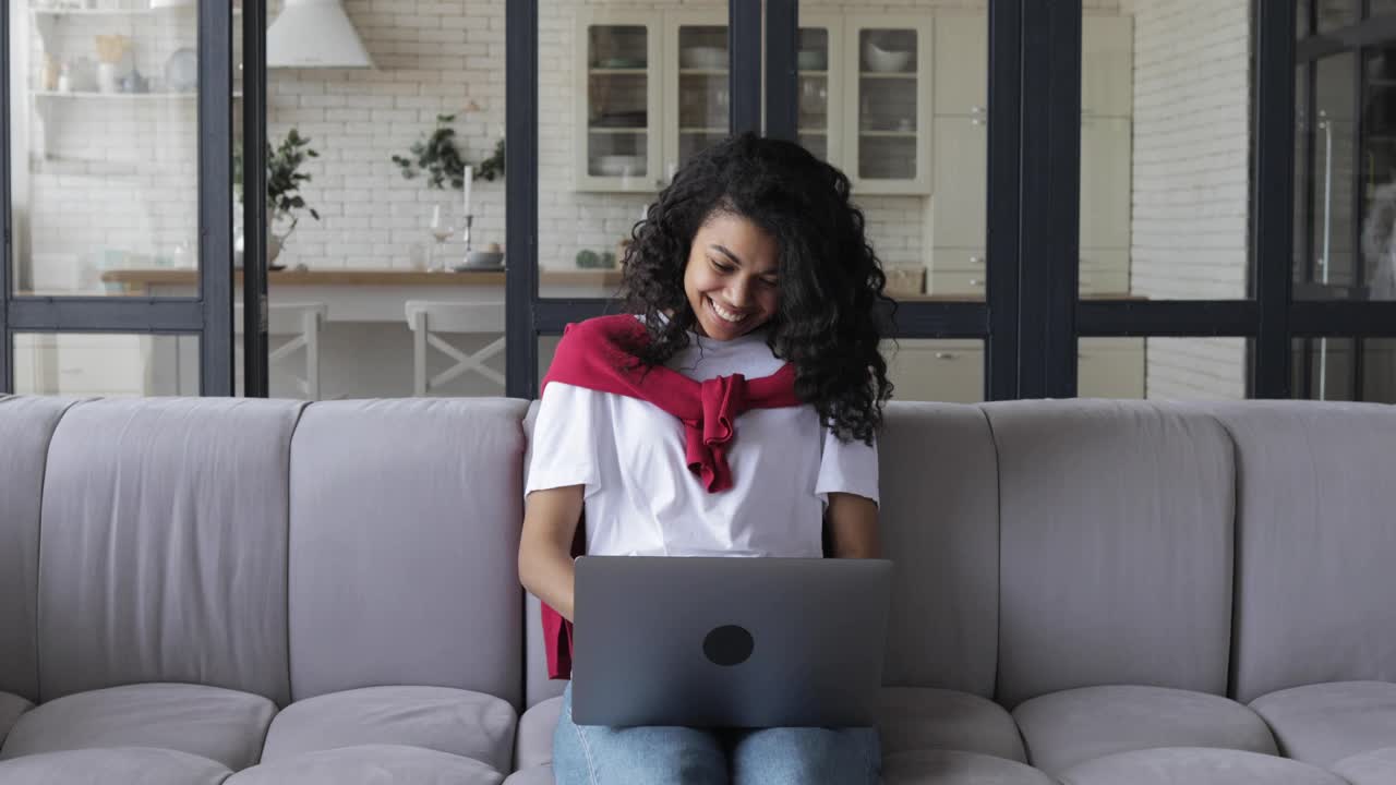 年轻的非洲裔美国女学生或自由职业者与卷发，工作或学习远程在家里使用笔记本电脑视频电话，在一个在线会议与同事交谈视频下载