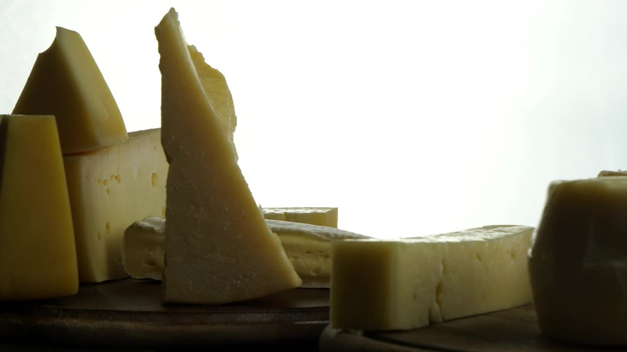 静物不同类型的奶酪在木板上，意大利高根佐拉，帕尔马干酪，法国布里干酪，奶酪在木板上缓慢旋转的视频视频下载