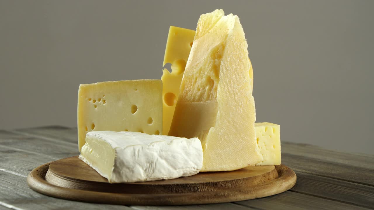不同种类的奶酪，法国布里干酪，瑞士奶酪，意大利帕尔马干酪，一组奶酪切片放在圆形木砧板上视频下载