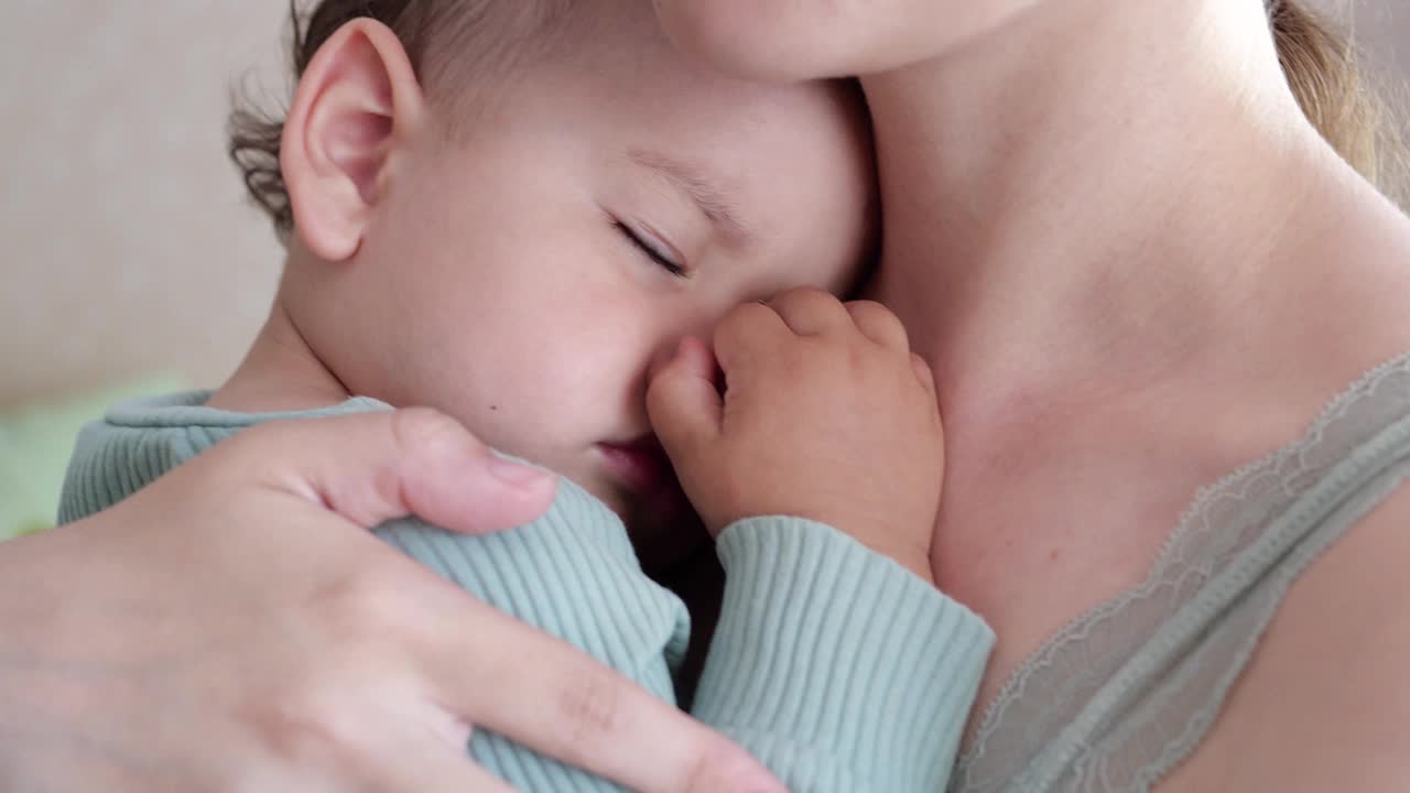 母亲在家里抱着熟睡的儿子，摇着他。男孩睡在妈妈的怀里视频素材