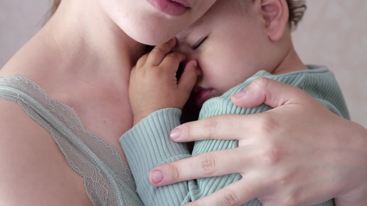 母亲在家里抱着熟睡的儿子，摇着他。男孩睡在妈妈的怀里视频素材
