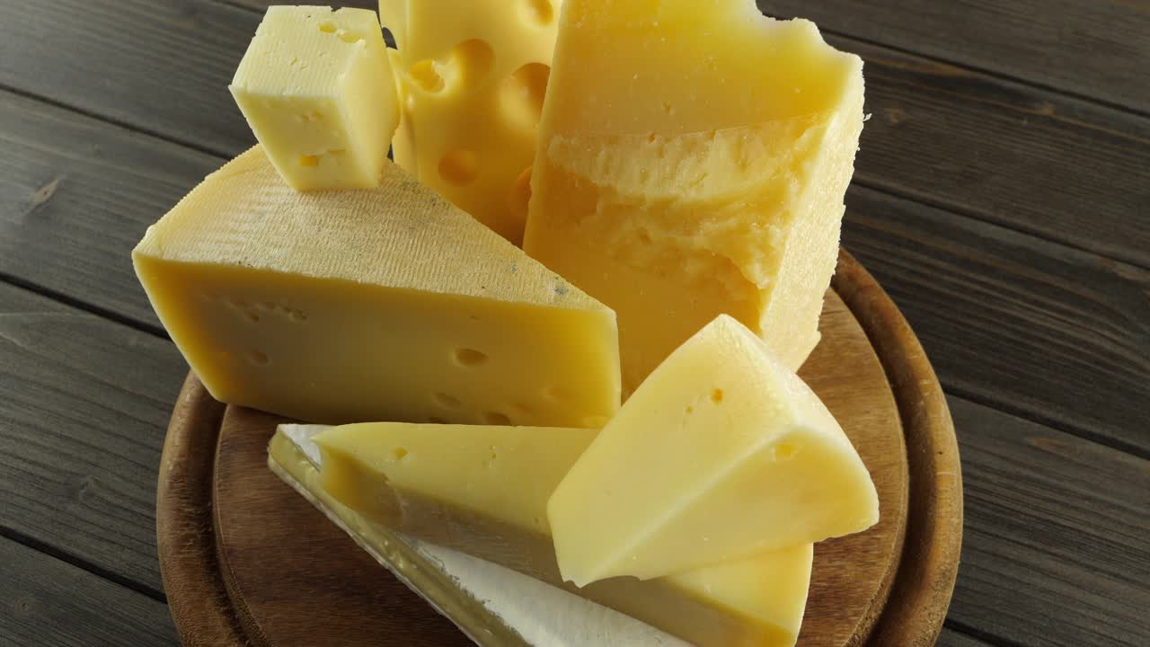 各种奶酪放在木砧板上，各种形状的奶酪切片放在木桌上，慢动作视频中缓慢旋转，瑞士奶酪，法国布里干酪，帕尔马干酪，意大利奶酪视频下载