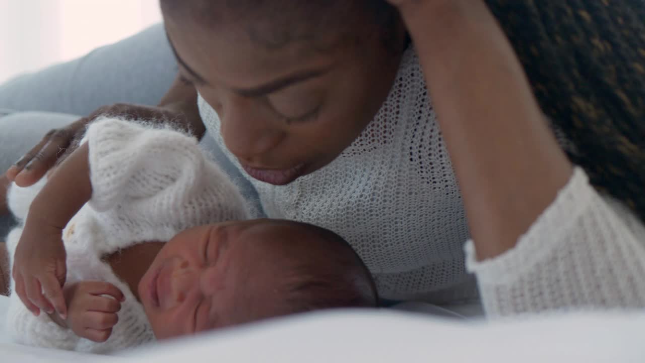 一位非洲裔单亲妈妈的爱，在家里亲吻她刚出生的孩子。一个哺乳婴儿的母亲。怀孕和生育的概念。视频素材