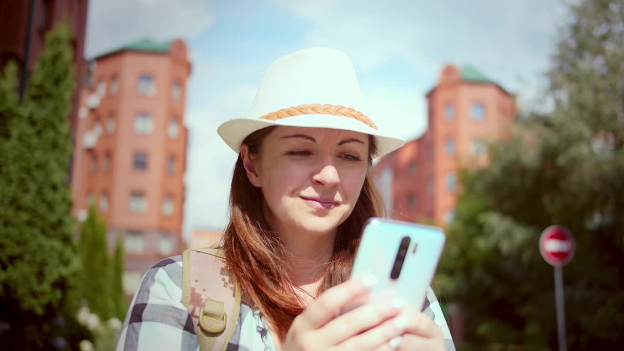 漂亮的女人戴着帽子，在红房子和微笑的背景下和朋友聊天，女人在夏天的好心情，机架焦点，电影拍摄视频素材