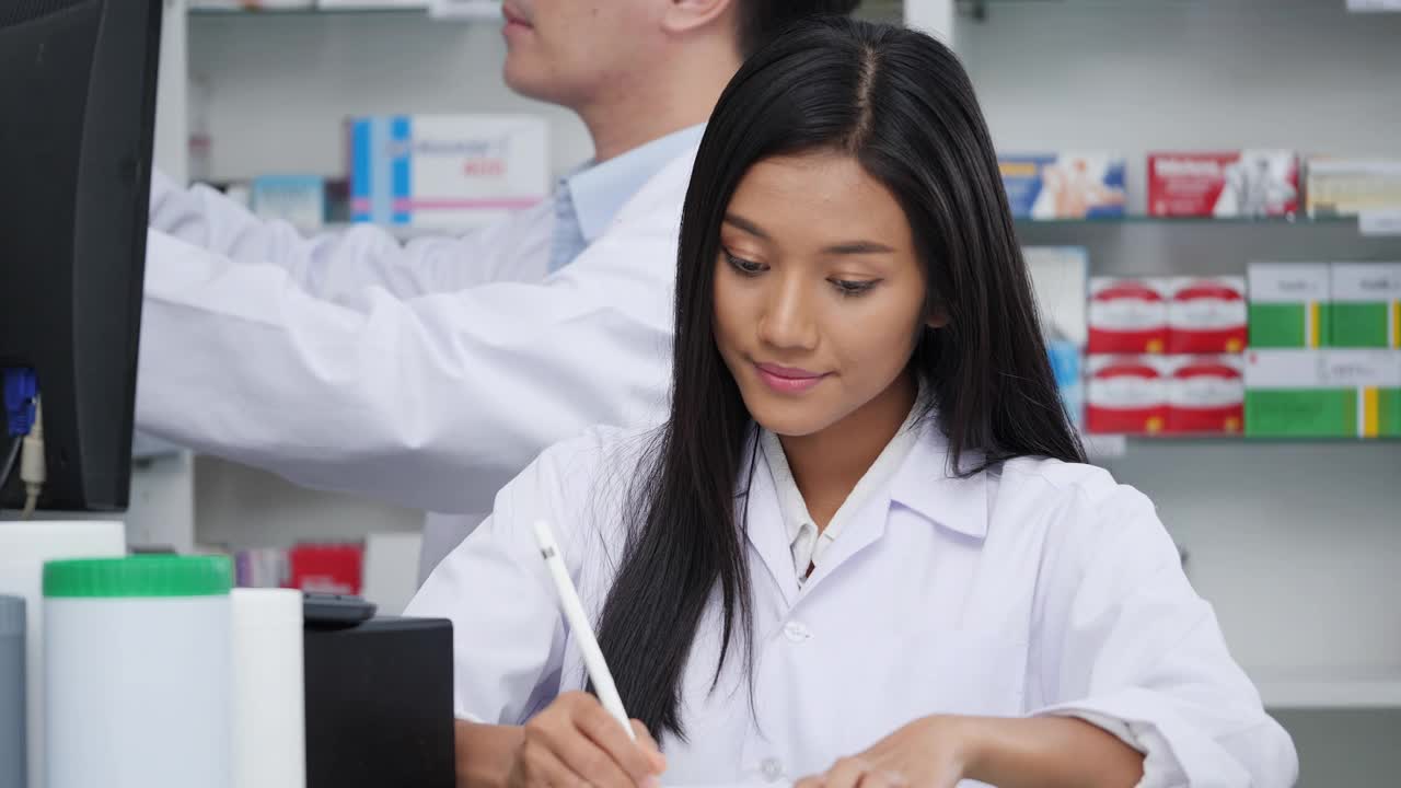 药剂师在医院药房工作、验药。亚洲医生正在检查药片上的药物数据，穿着医疗外套。有药店药学背景的货架。视频素材