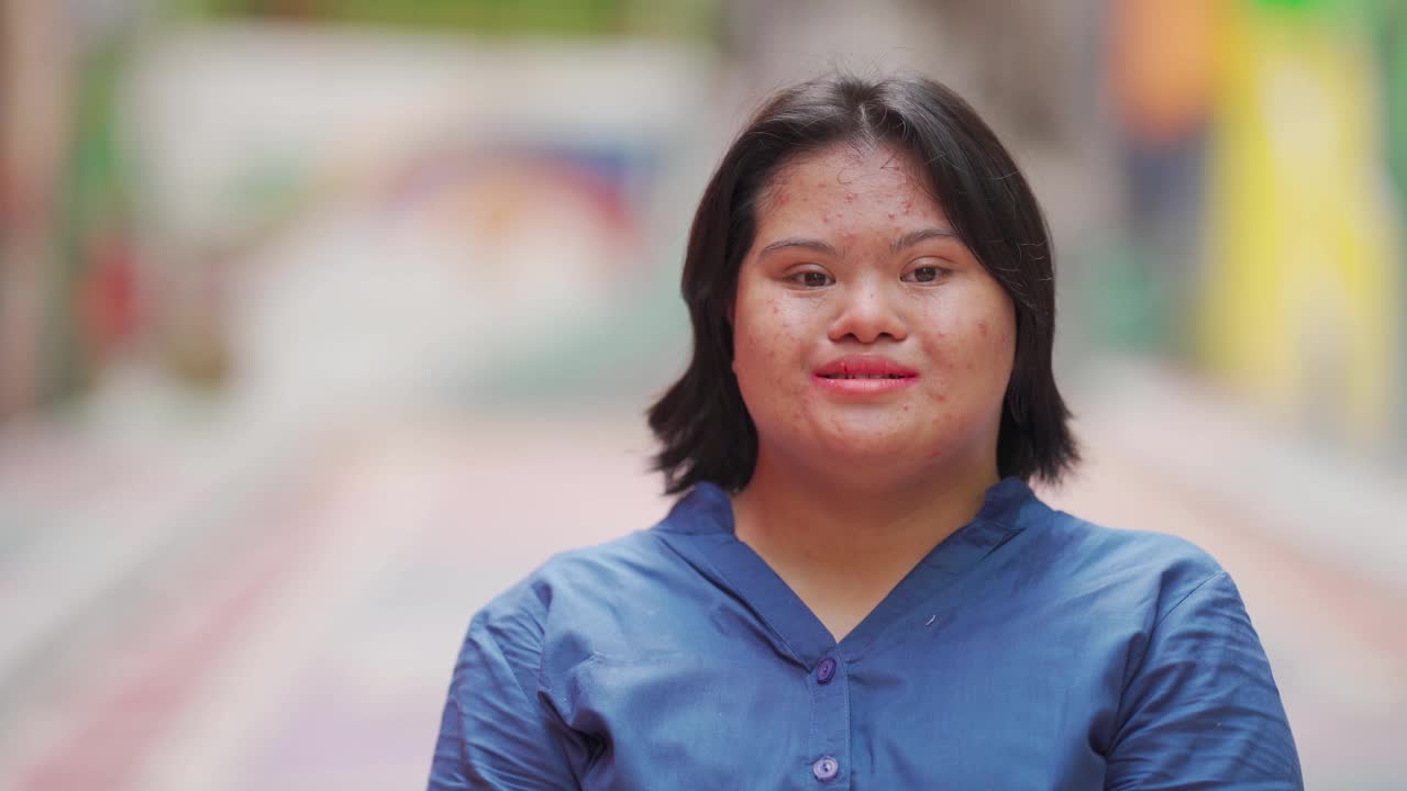 快乐的亚洲马来人自闭症唐氏综合症女性看镜头微笑在城市街道视频下载