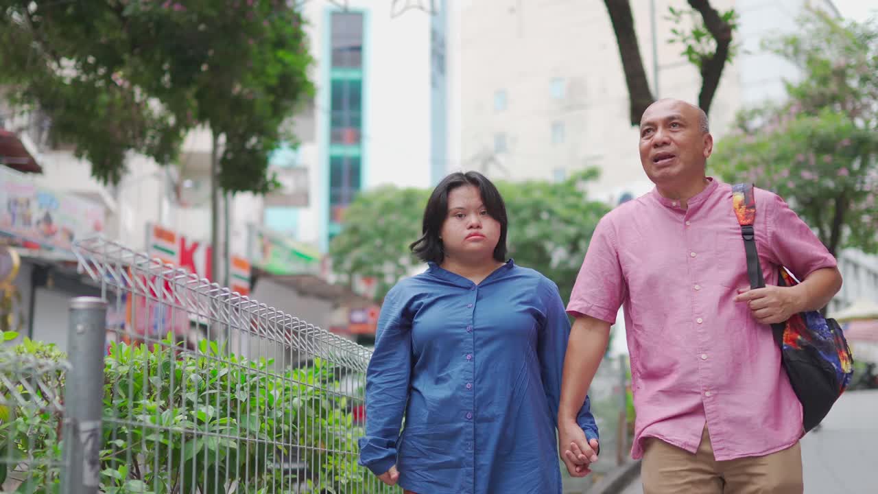 亚洲马来退休父亲和他的唐氏综合症的女儿手牵手走在城市街道在周末休闲活动视频素材