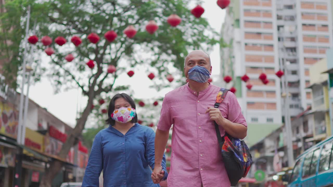 亚洲马来退休父亲和他的唐氏综合症的女儿在周末的休闲活动中手牵着口罩穿过城市街道视频下载