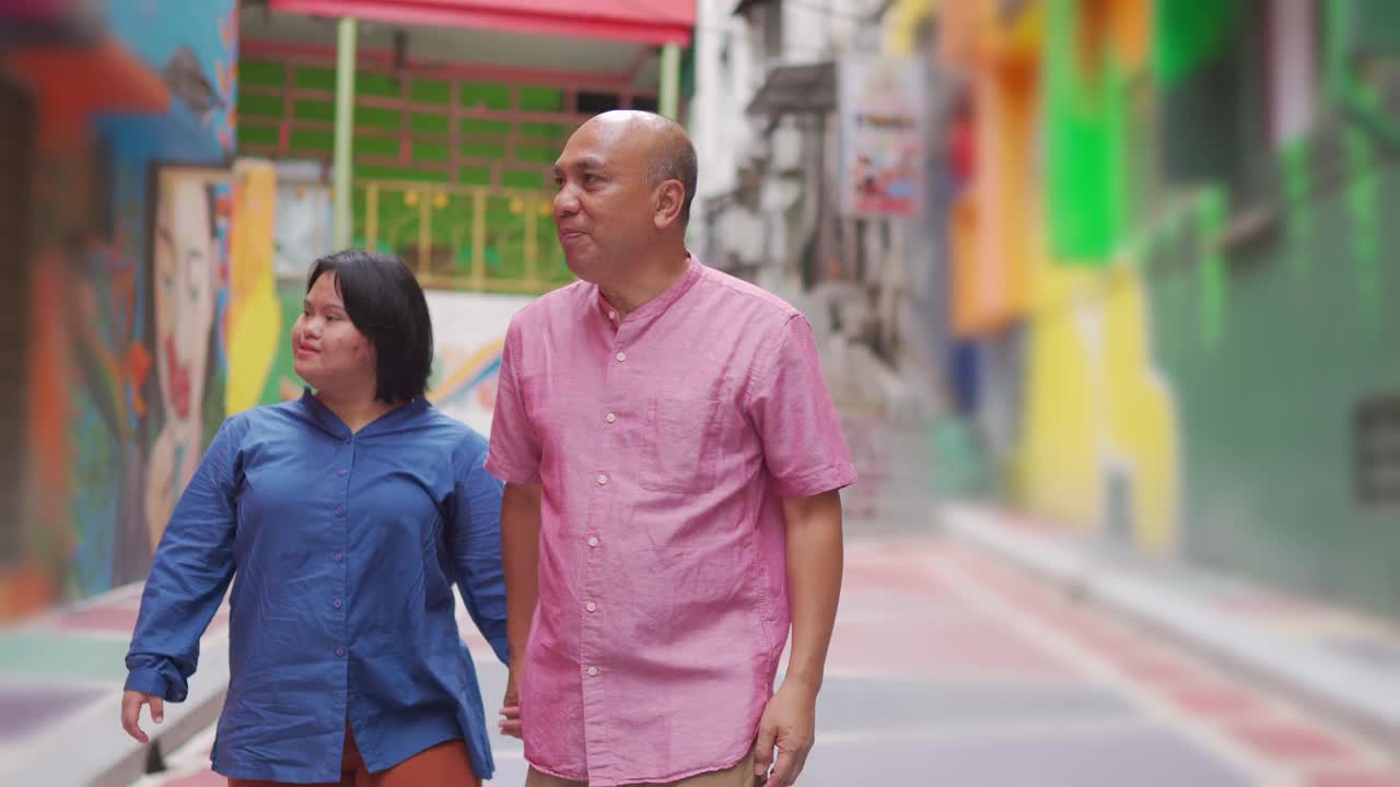 亚洲马来退休父亲和他的唐氏综合症的女儿手牵手走在城市街道在周末休闲活动视频素材
