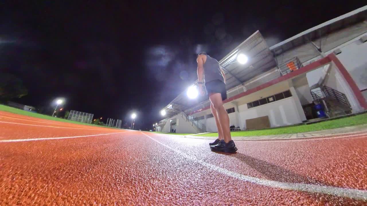 后视图空气动力学亚洲中国男运动员在跑道上冲刺，向终点线在田径体育场，雨深夜跟踪射击视频下载