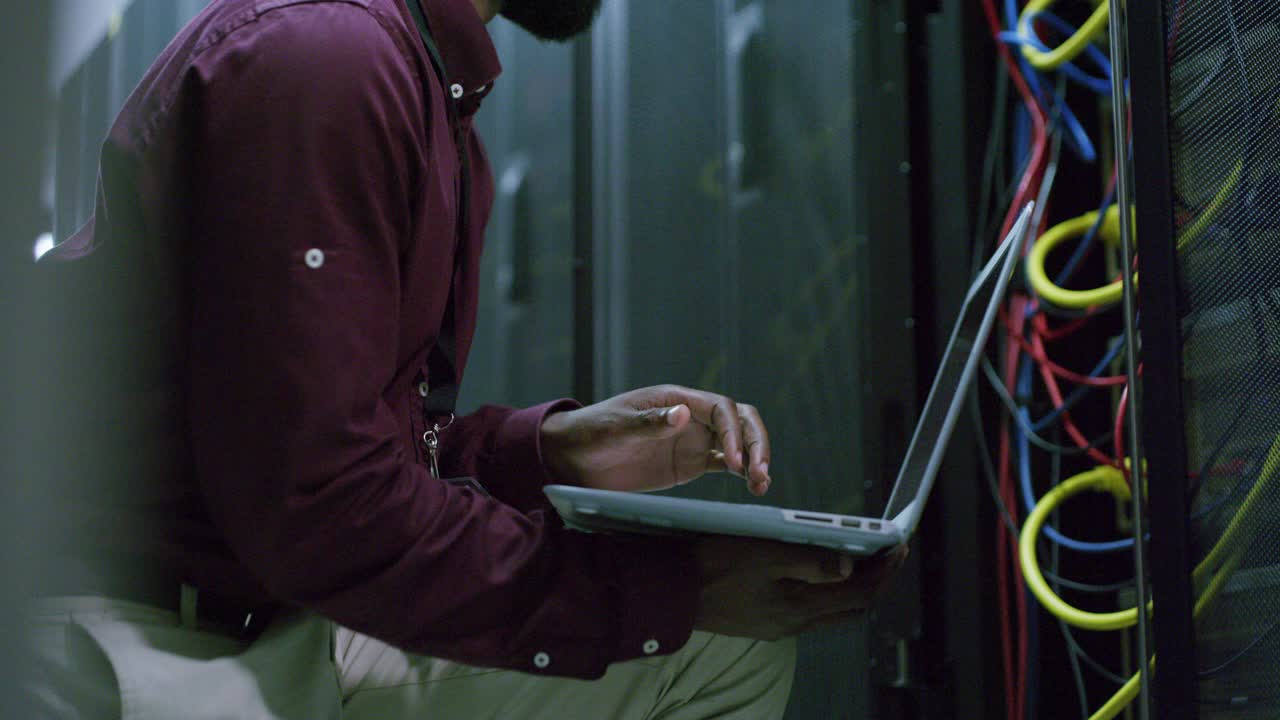 一个年轻人在服务器室工作时用笔记本电脑的4k视频片段视频素材