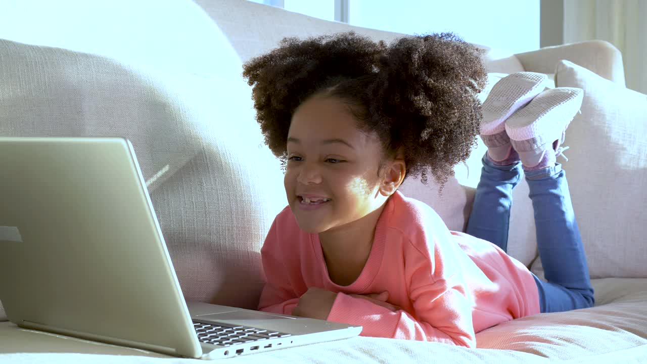 非裔美国女孩坐在沙发上用笔记本电脑视频下载