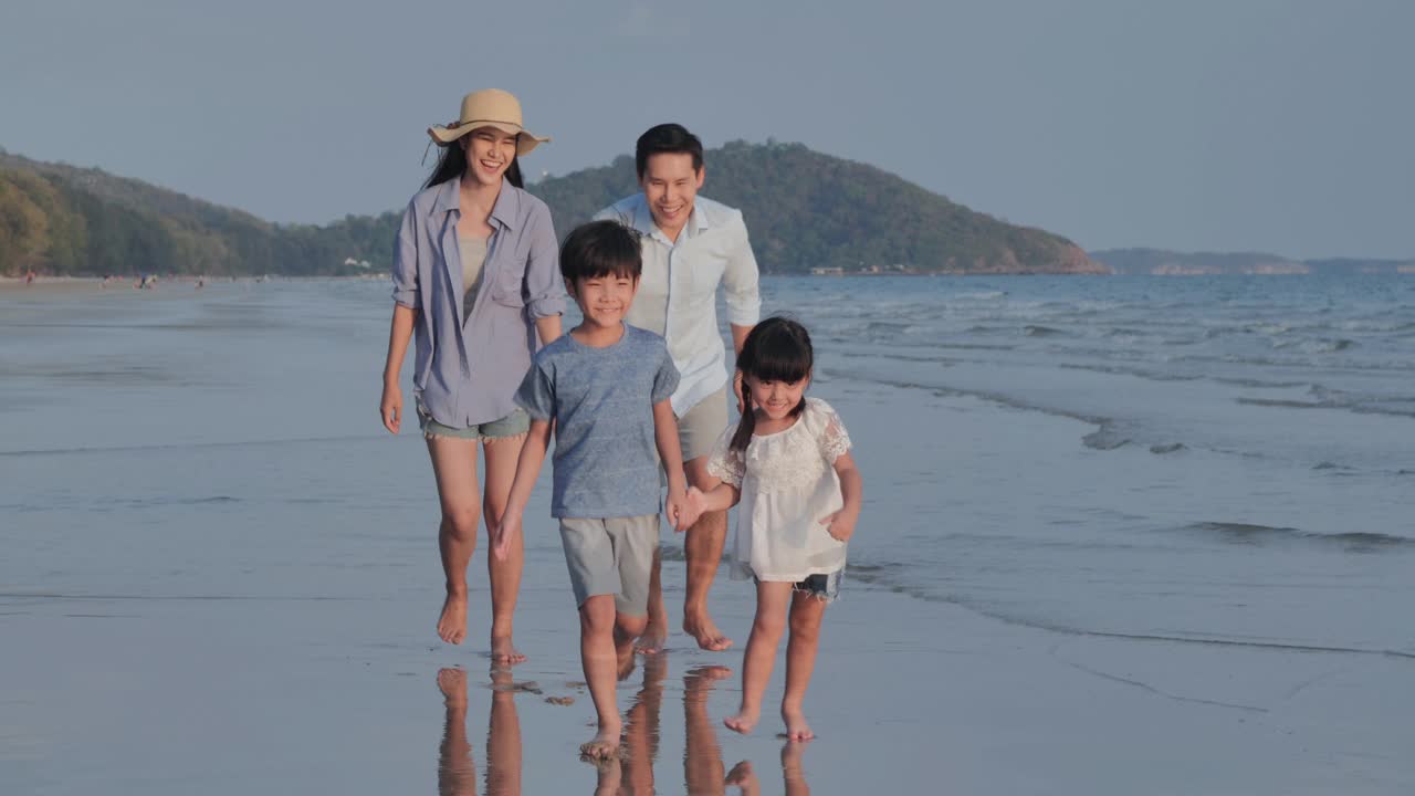 幸福的亚洲家庭的爸爸，妈妈和4-8岁的男孩和女孩手牵着手在海边的沙滩上快乐地奔跑。积极的父母和人们在热带夏季假期户外活动的孩子。援助之手的概念。视频下载