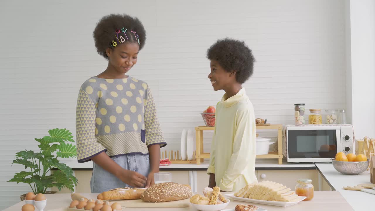 两个可爱可爱的兄弟姐妹，非洲裔美国孩子在厨房喝着牛奶吃早餐，快乐的兄弟和他的妹妹喝牛奶的画像，竖起大拇指，食物和饮料的概念视频素材