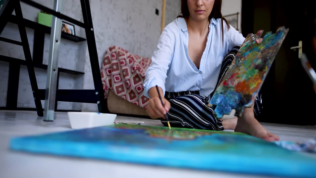 一个年轻漂亮的女人在她画室的地板上画画视频下载