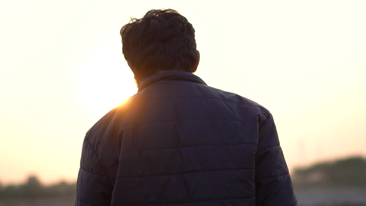 一个印度人在日落时走在太阳前面的肖像。孤独的人在夕阳下散步。孤独的概念。人独自行走，思考他的未来。视频下载