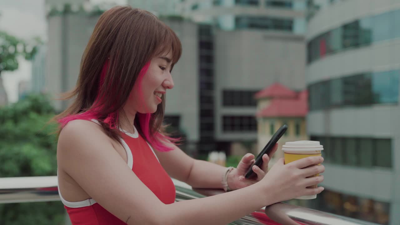微笑的年轻女子在城市里用智能手机看风景视频下载