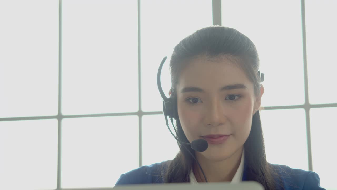 美丽友好的亚洲女性呼叫中心工作，通过耳机与客户交谈。微笑的年轻员工客户支持操作员工作。咨询和协助服务呼叫中心。视频素材
