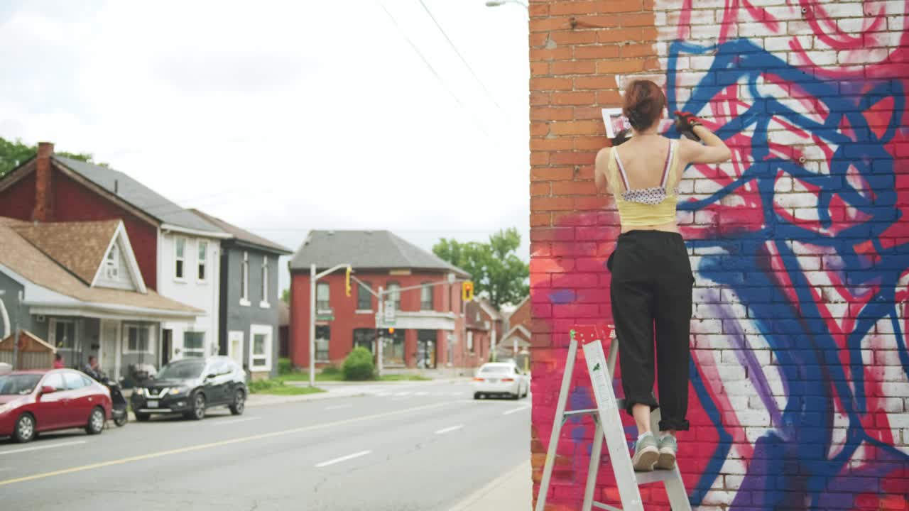 一个年轻女人在房子上画壁画视频素材