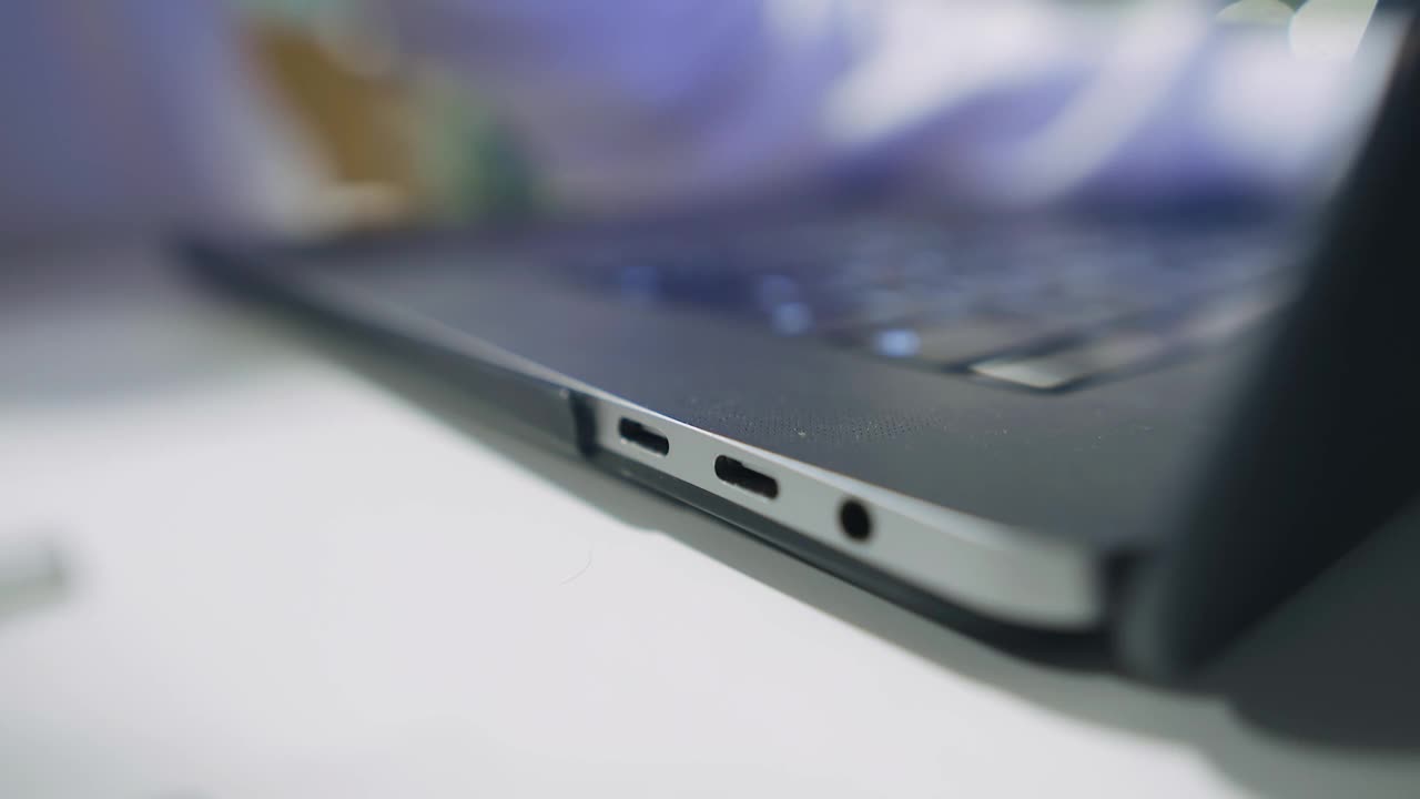 一个人将一个白色插头从侧面插入笔记本电脑接口。近距离射击视频素材