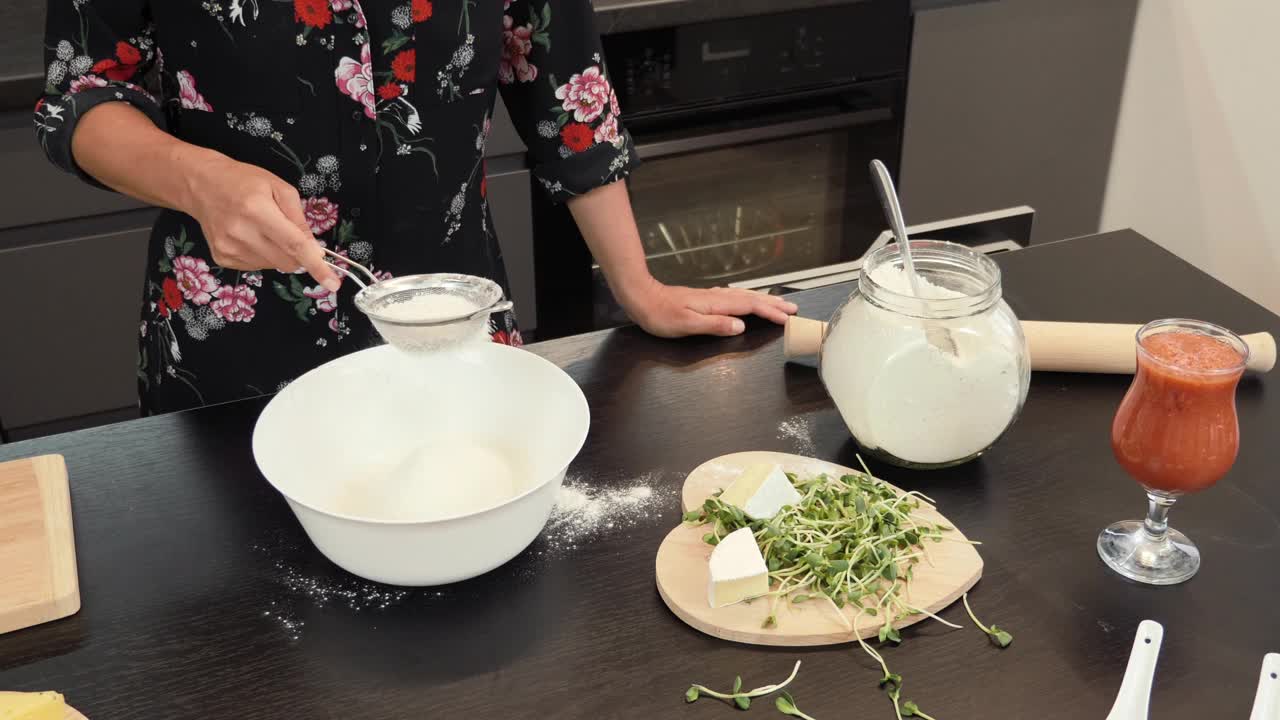 用筛子筛面粉，慢动作。在现代家庭厨房里，妇女为意大利披萨准备传统面团。制作披萨的过程。女性在家庭厨房为家人做饭视频素材