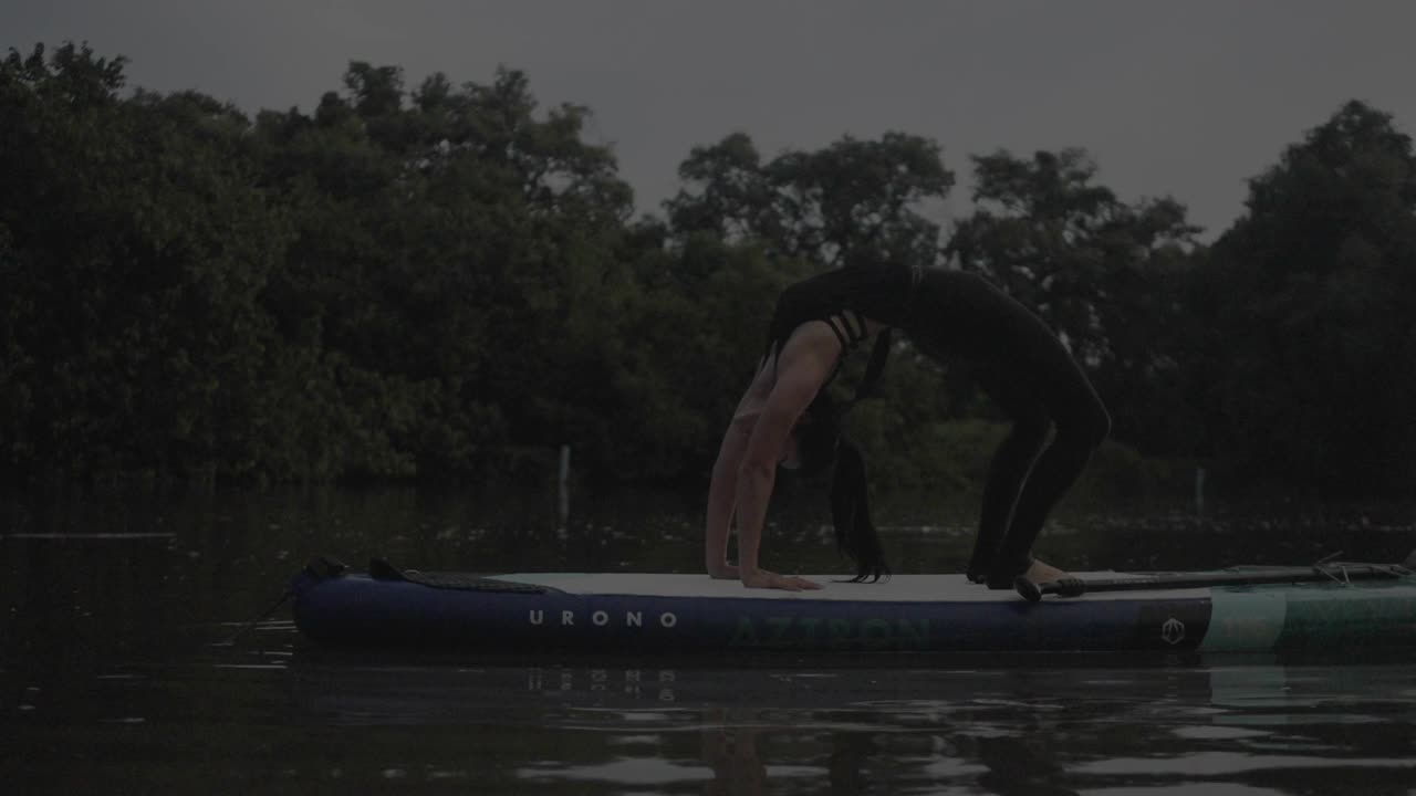 一名女子在湖上站立式桨板上练习瑜伽。视频下载