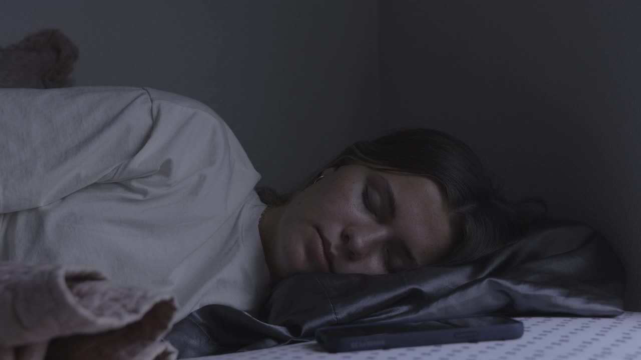 女孩睡觉在床上醒来和恼怒的手机闹钟/普罗沃，犹他州，美国视频下载