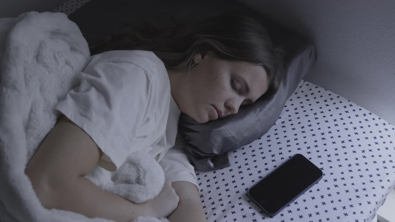 女孩睡在床上被手机闹钟吵醒的高角度视角/美国犹他州普罗沃视频下载