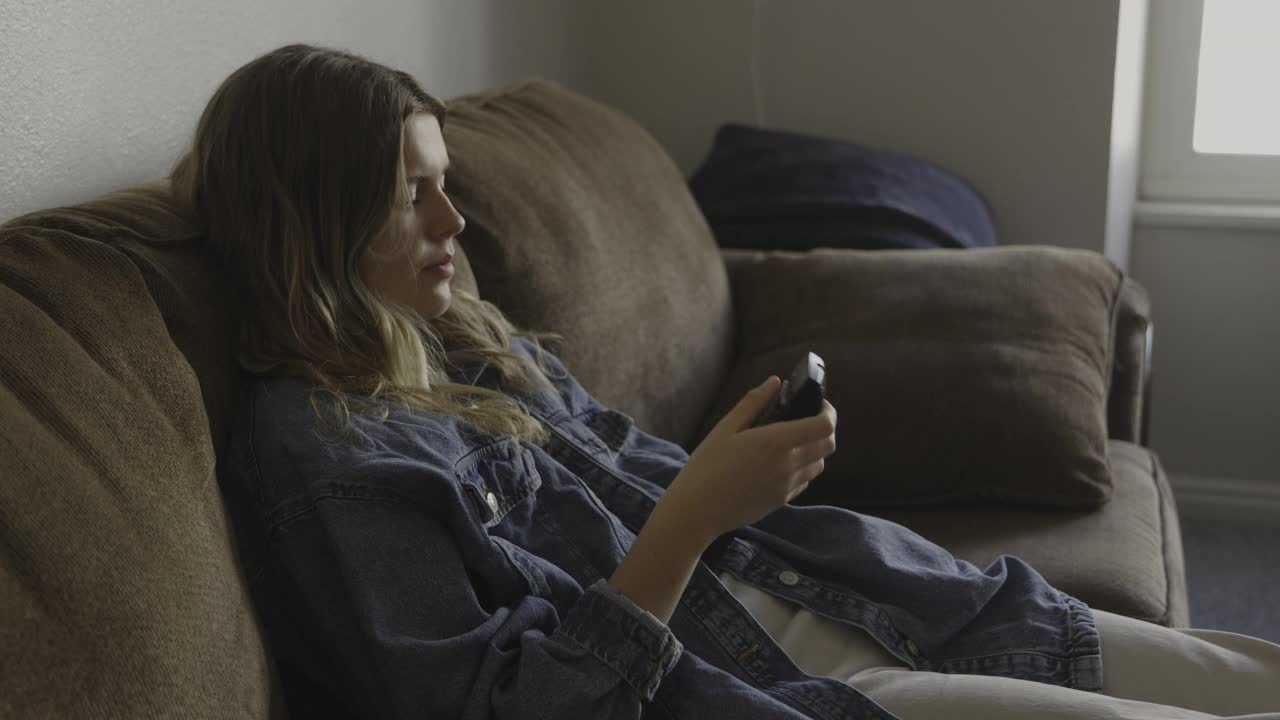 女孩坐在沙发上用遥控器看电视/普罗沃，犹他州，美国视频素材