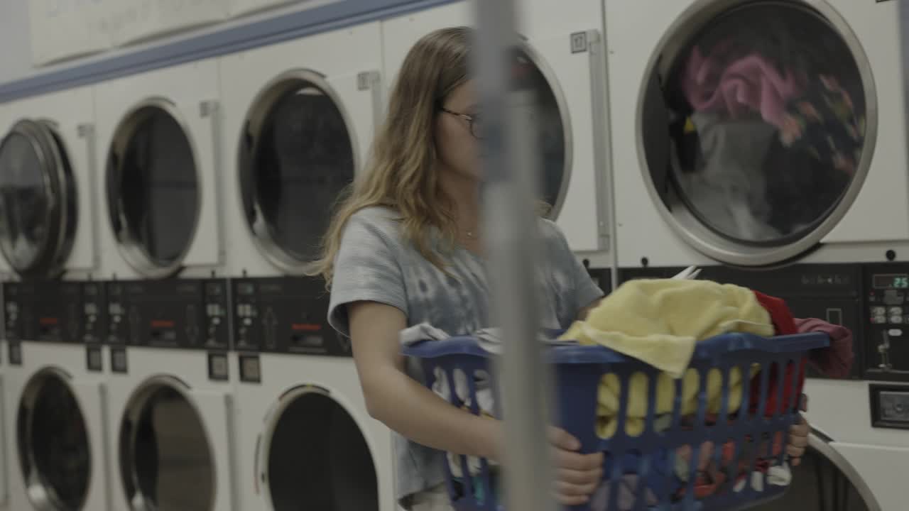 女孩提着洗衣篮在自助洗衣店看书/普罗沃，犹他州，美国视频素材