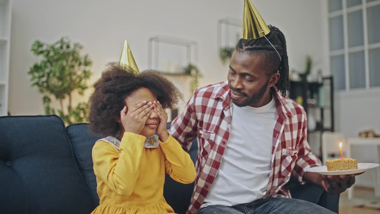 可爱的非洲父亲戴着派对帽给女儿送生日蛋糕视频素材