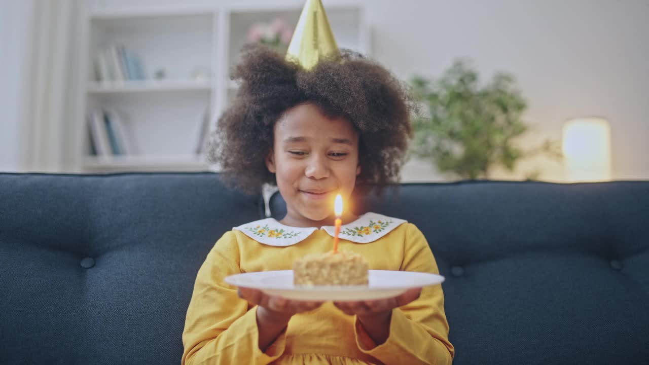 欢快的美国黑人女孩在生日蛋糕上吹蜡烛，庆祝节日视频素材