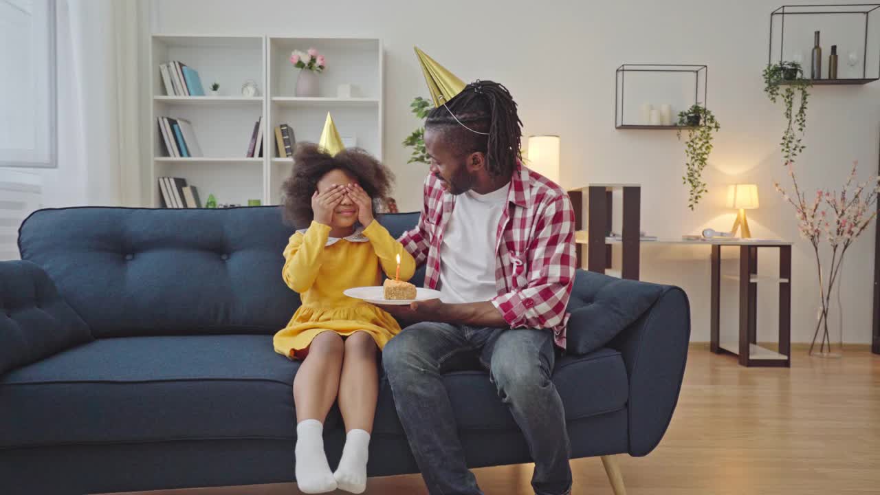 戴着派对帽的非洲爸爸给女儿送上生日蛋糕视频素材