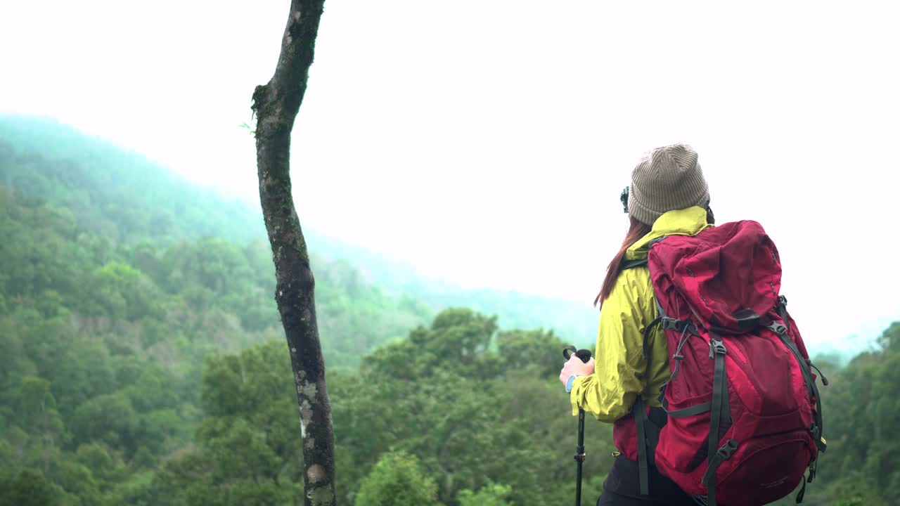 亚洲探险家，冒险爱好者，女性背包客站在绿色的热带森林在恶劣的天气下，拍摄全景景观，显示白色的天空雾视频素材