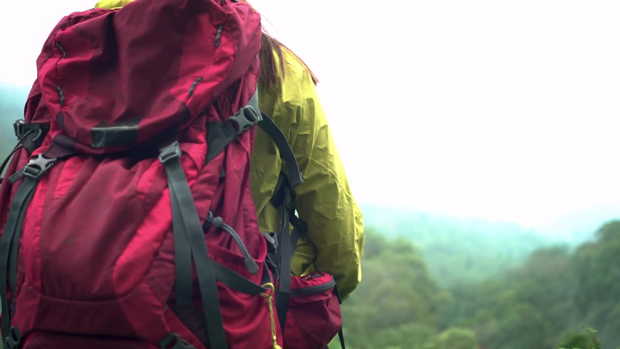 亚洲探险家，冒险家，女性背包客，作为情人独自徒步旅行的成功举起手臂，在恶劣的天气下，在热带森林的山顶上，在泰国的雨季，雾覆盖了所有山峰，包括下雨，寒风。视频素材