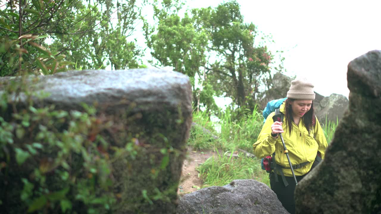 大头照视图:亚洲探险家、冒险家、女背包客沿着大石攀登，在恶劣天气下作为情人在热带森林徒步旅行，在泰国雨季到达顶峰，雾覆盖山顶的所有区域视频素材