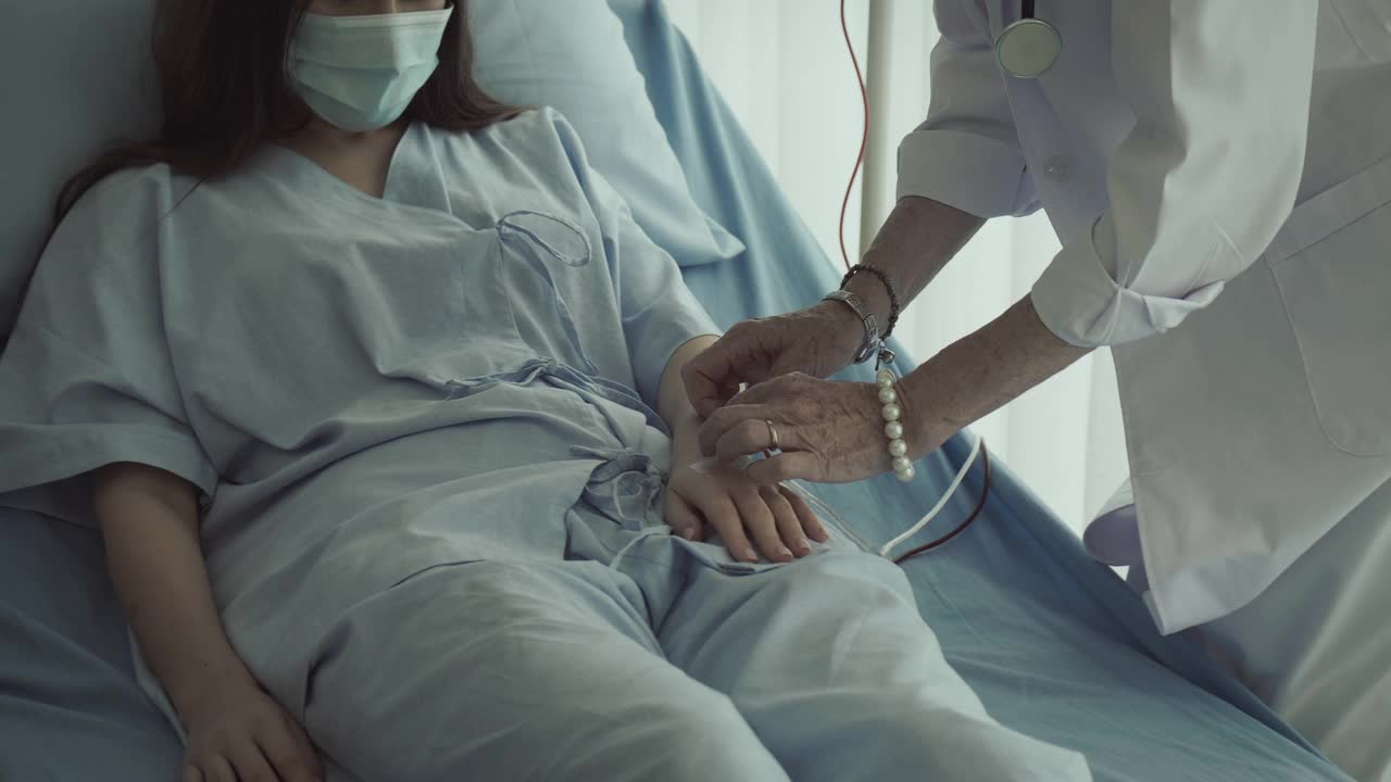 一位女病人躺在病床上，与她的资深医生讨论处方药物的选择。医生回答病人的问题。他们戴着防护口罩。视频素材