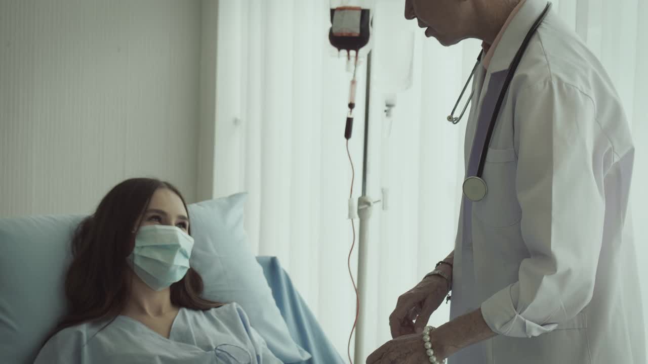一位女病人躺在病床上，与她的资深医生讨论处方药物的选择。医生回答病人的问题。他们戴着防护口罩。视频下载