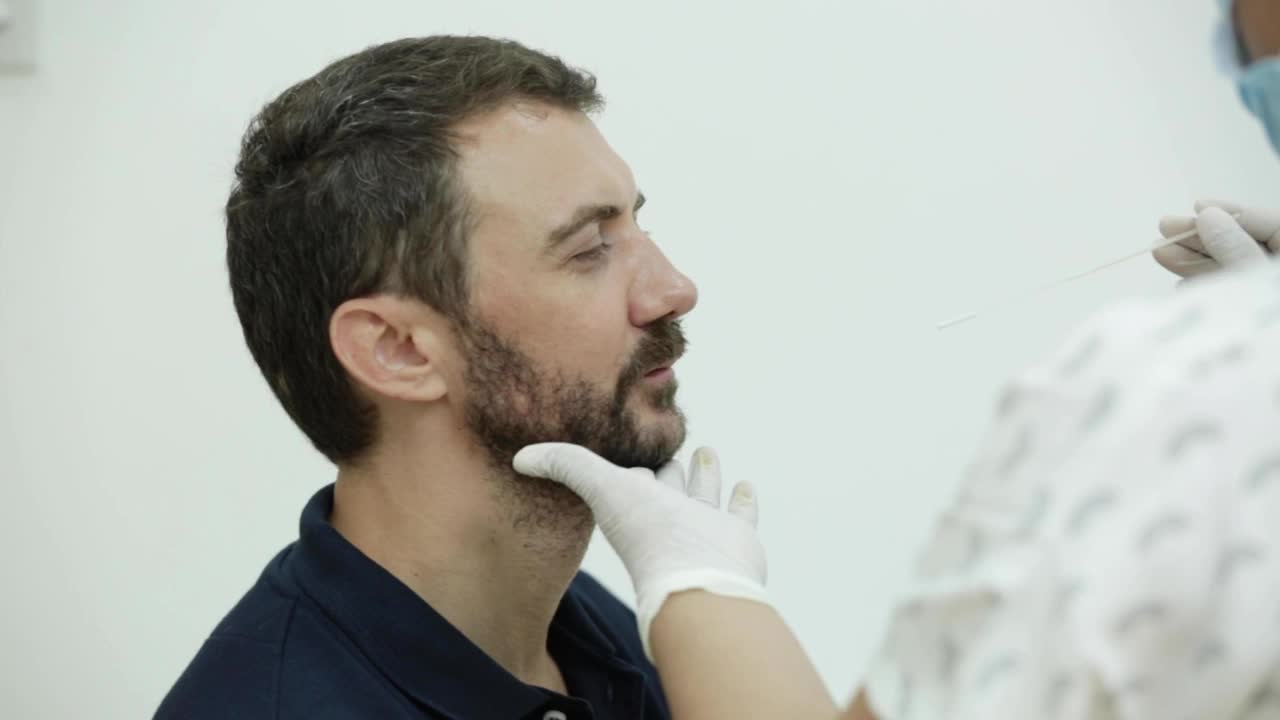 冠状病毒检测——医护人员从年轻胡须男子的鼻腔快速拭子中提取冠状病毒样本视频素材