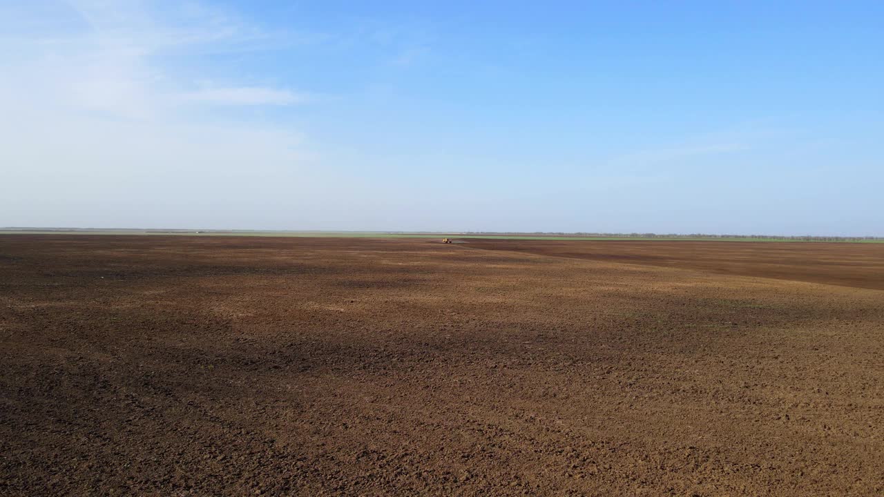 一望无际的棕色田野与农用拖拉机的剪影和漂浮的乌云阴影下的蓝天在春日鸟瞰图视频下载