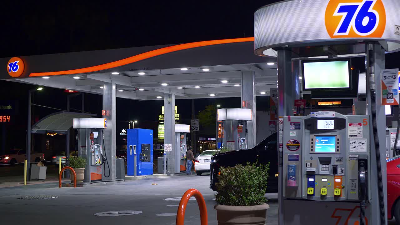 76个品牌汽油标志性的橙色球标志和顾客在加州洛杉矶的加油站加油，晚上，4K视频下载
