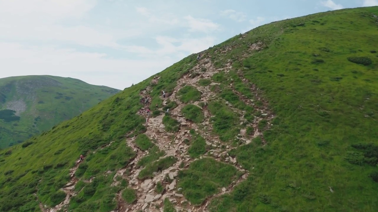 鸟瞰图一群年轻的游客沿着山路走到山顶。视频下载