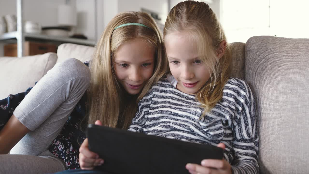 两个小女孩坐在家里用数字平板电脑的4k视频片段视频下载