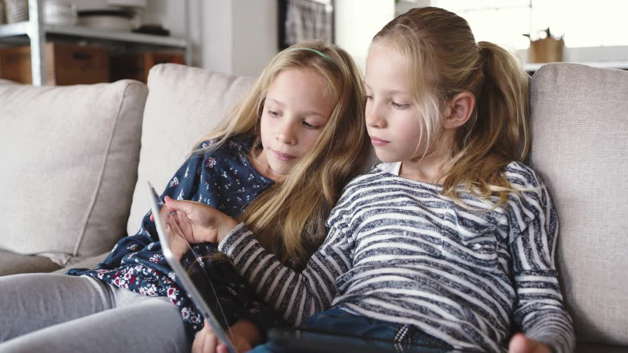 两名年轻女孩坐在家里使用数码平板电脑的4k视频片段视频下载