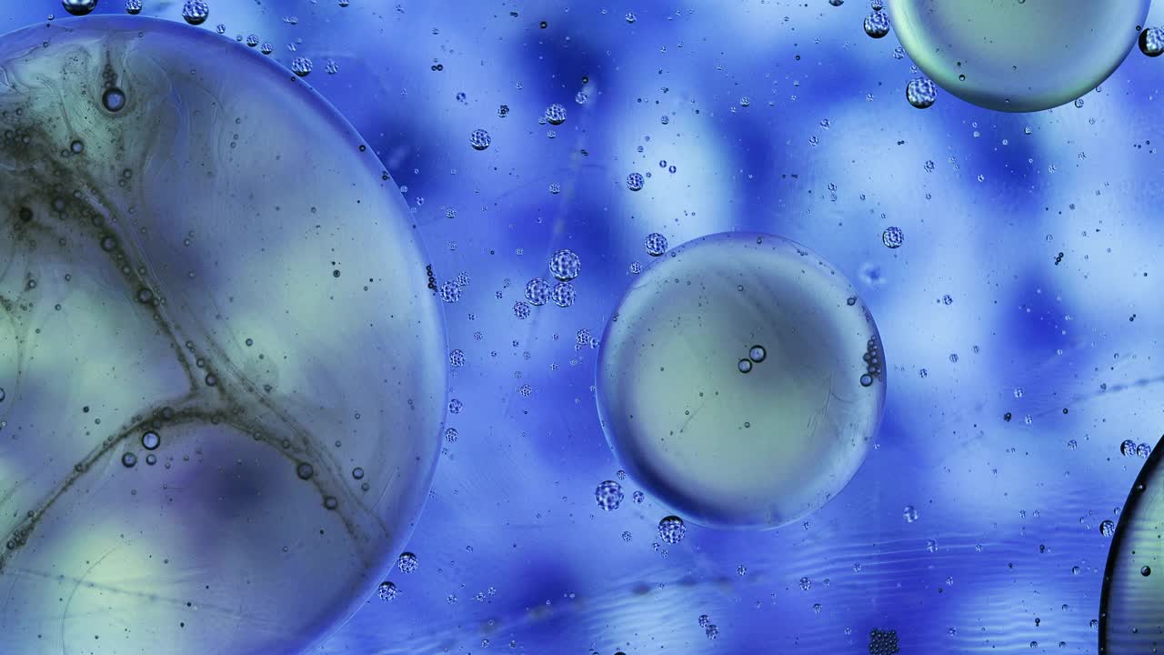 一个行星形状的液体气泡，漂浮在蓝色液体的表面。视频素材