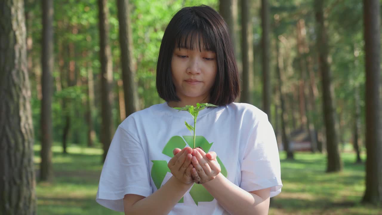关爱自然，年轻的亚洲女志愿者手中拿着一株小花，看着镜头，一个隐喻的动作，大自然就在我们手中，慢动作。视频素材